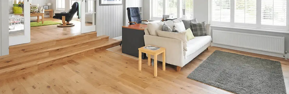 A modern living room with professionally installed laminate flooring, a beige sofa, a small side table, a gray rug, and large windows with white shutters in Eugene, OR